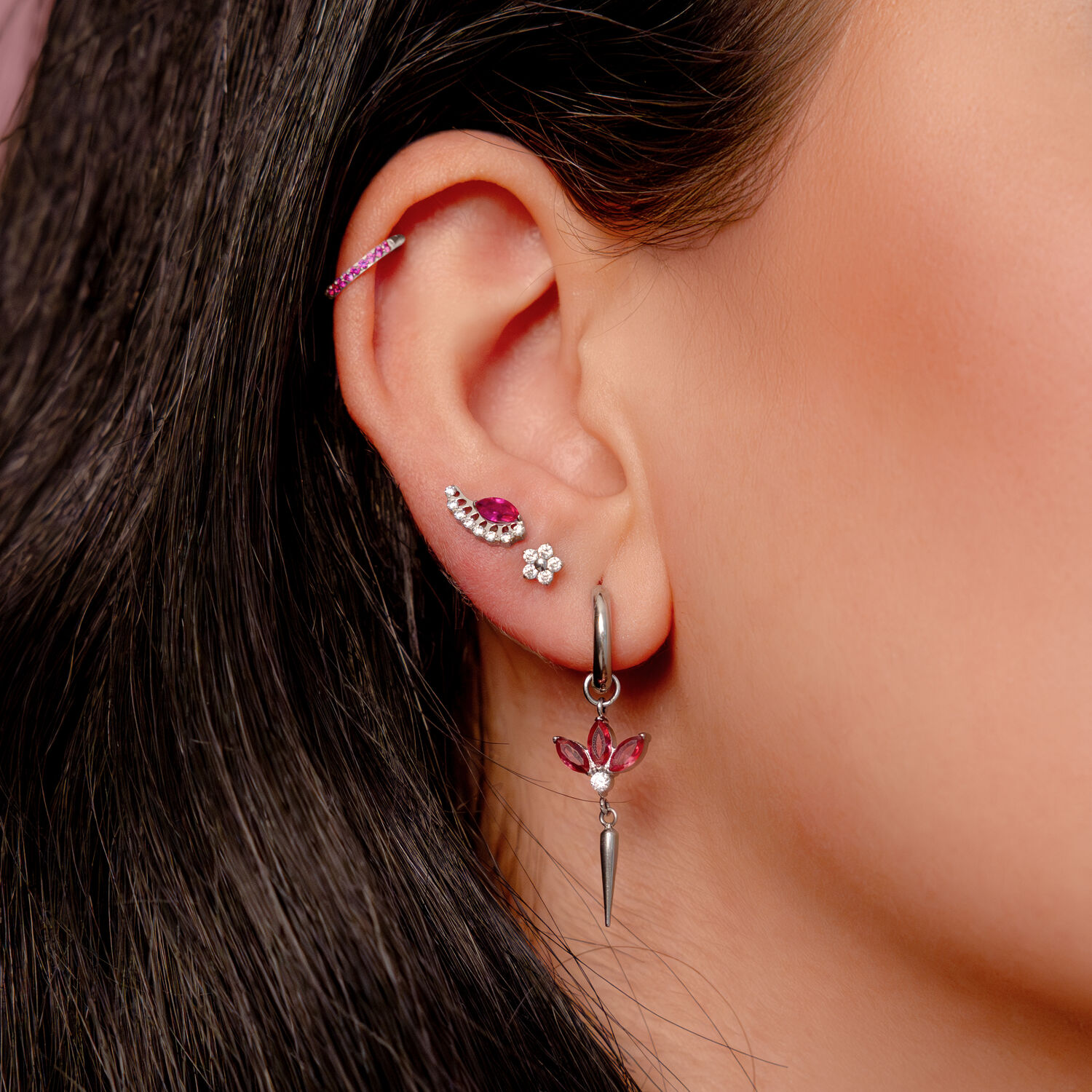 Pendiente de plata en la oreja con cristales rojos y varios piercings en una oreja