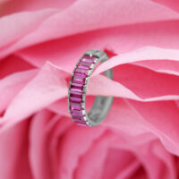 Anillo de piercing plateado con cristales baguette rojos sobre fondo de flores rosas