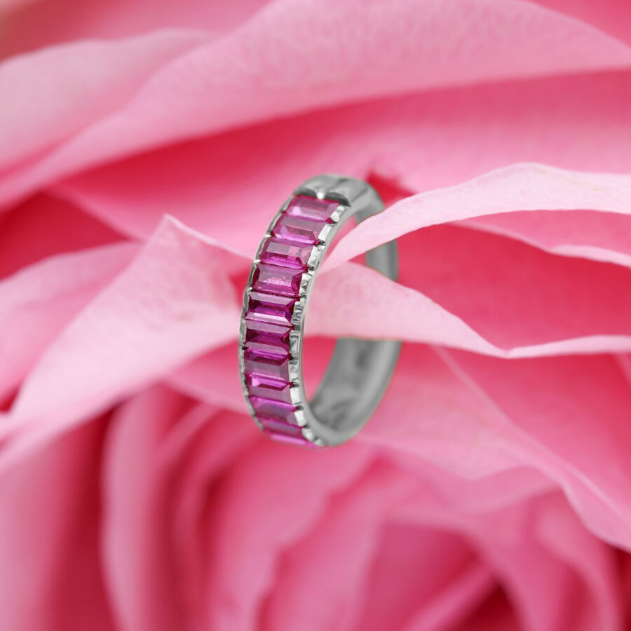 Anillo de piercing plateado con cristales baguette rojos sobre fondo de flores rosas
