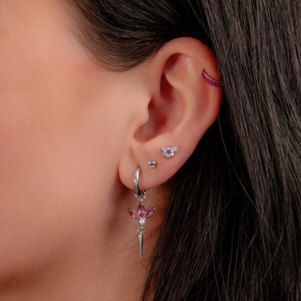 Oreja con varios piercings, incluyendo un clicker plateado con cristales rojos.