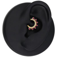 Pendiente dorado con cristales rojos colocado en un modelo de oreja negra