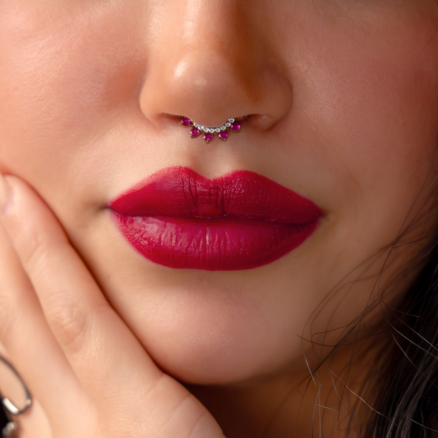 Primer plano de un clicker rojo con cristales rojos, usado en un septum nasal, rodeado de labios rojos.