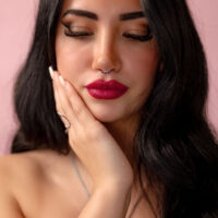 Mujer con ojos cerrados, lleva Piercing Clicker Ruby Red con Cristal Rojo, fondo rosa