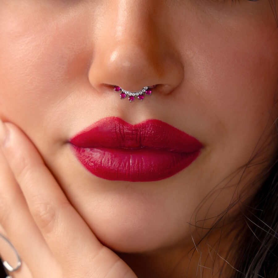 Primer plano de un rostro con piercing de septum plateado y cristales rojos