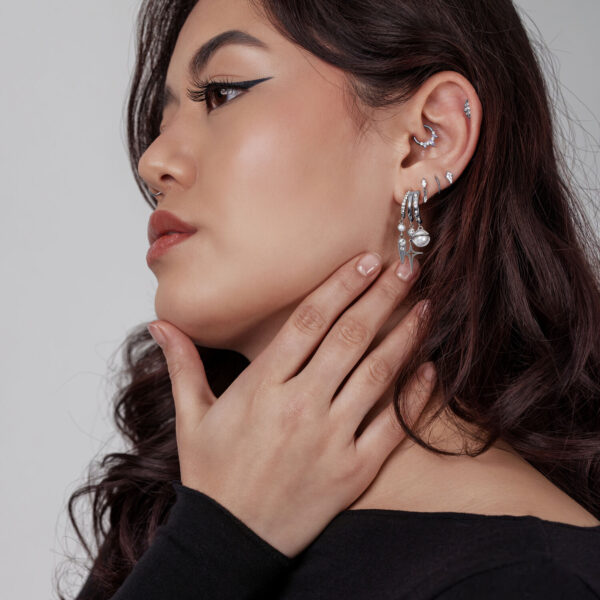 Mujer con varios pendientes y anillos plateados, perfil lateral