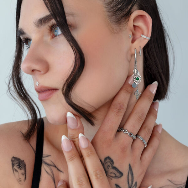 Mujer con pendientes de plata de ágata musgosa y tatuajes sobre fondo claro
