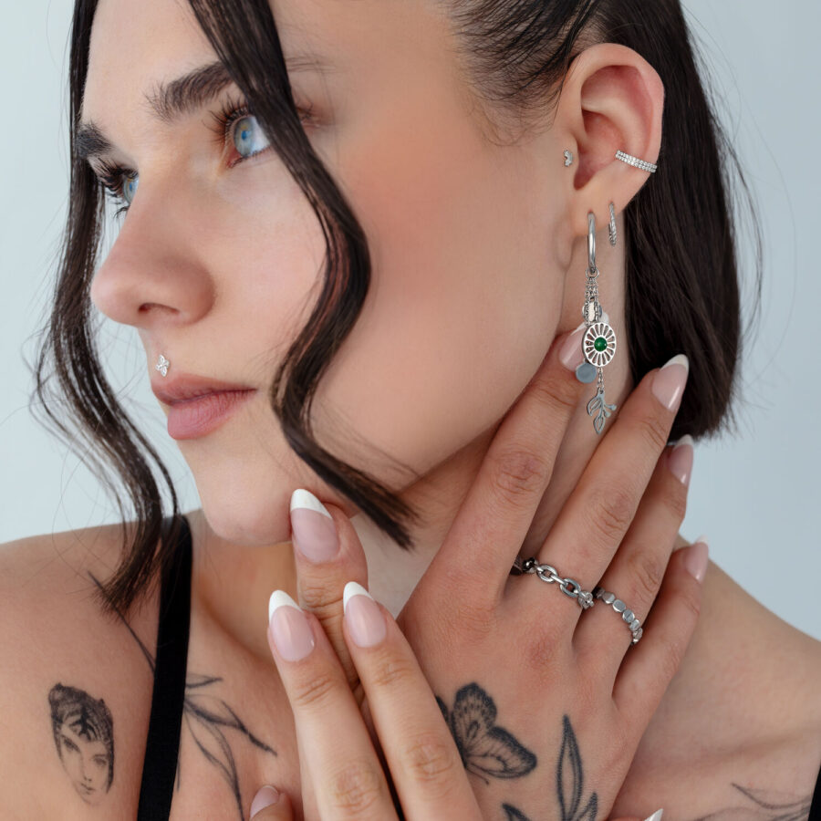 Mujer con pendientes de plata de ágata musgosa y tatuajes sobre fondo claro