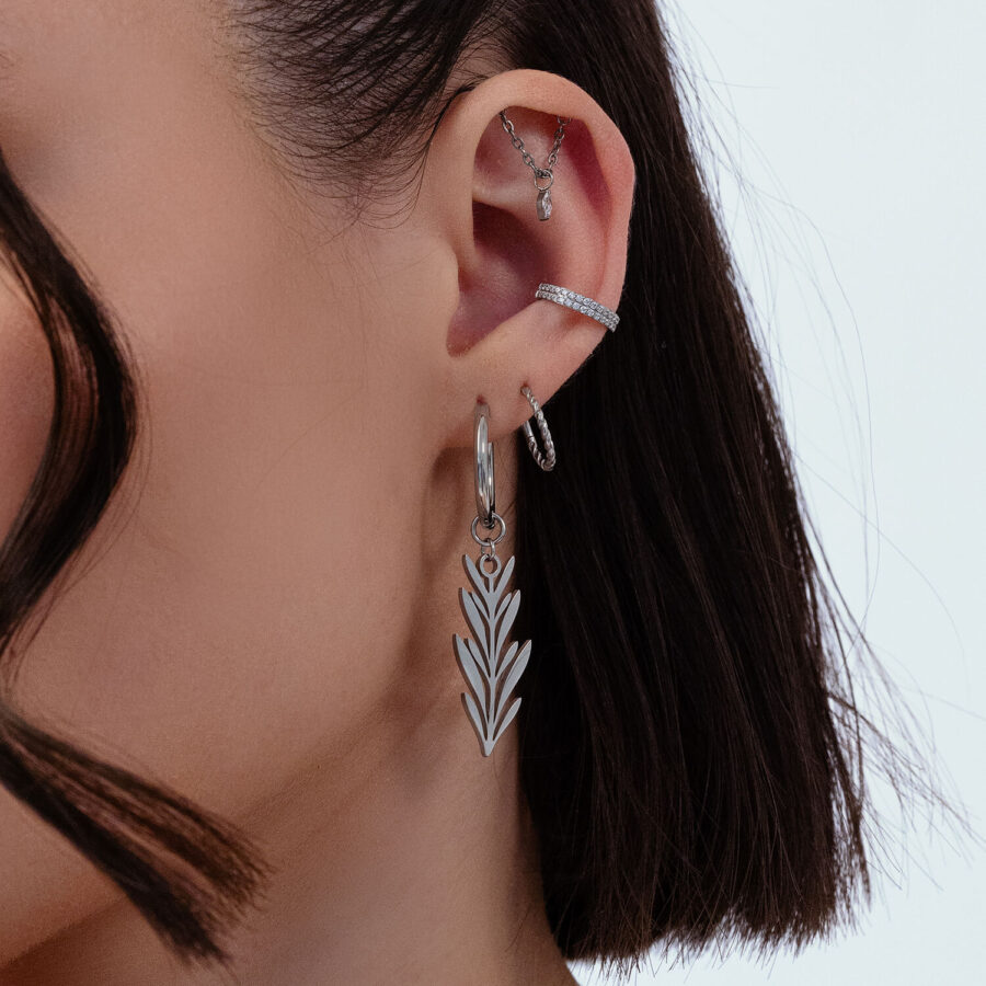 Primer plano de una oreja con pendientes plateados de diseño de hoja, varios piercings