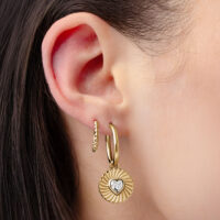 Pendientes dorados con colgante de corazón Pendientes dorados con colgante de corazón, llevados en una oreja, sobre fondo claro