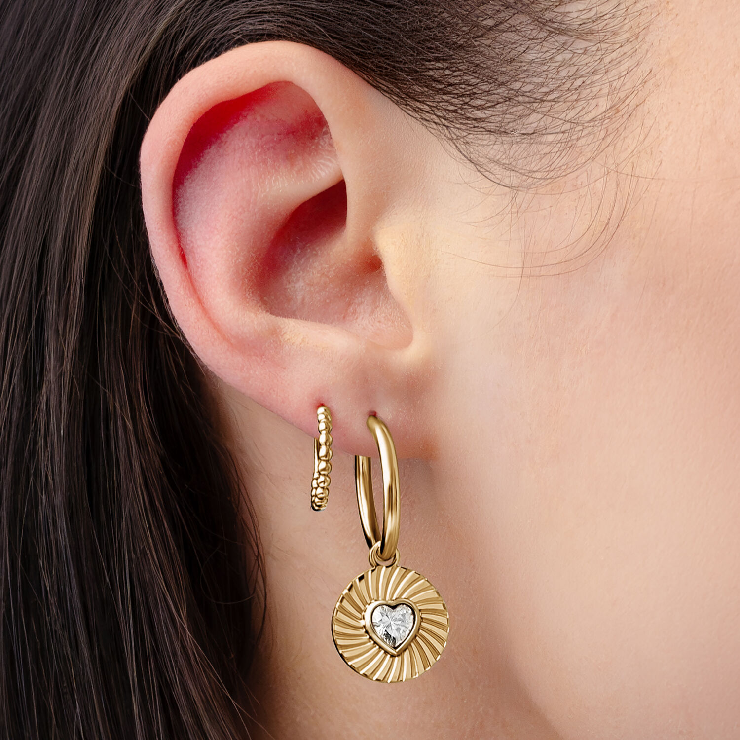 Pendientes dorados con colgante de corazón Pendientes dorados con colgante de corazón, llevados en una oreja, sobre fondo claro