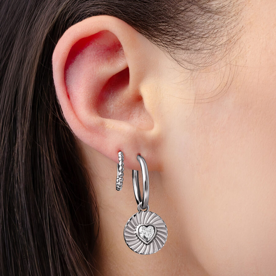 Aros plateados con colgante de corazón y cristal en una oreja