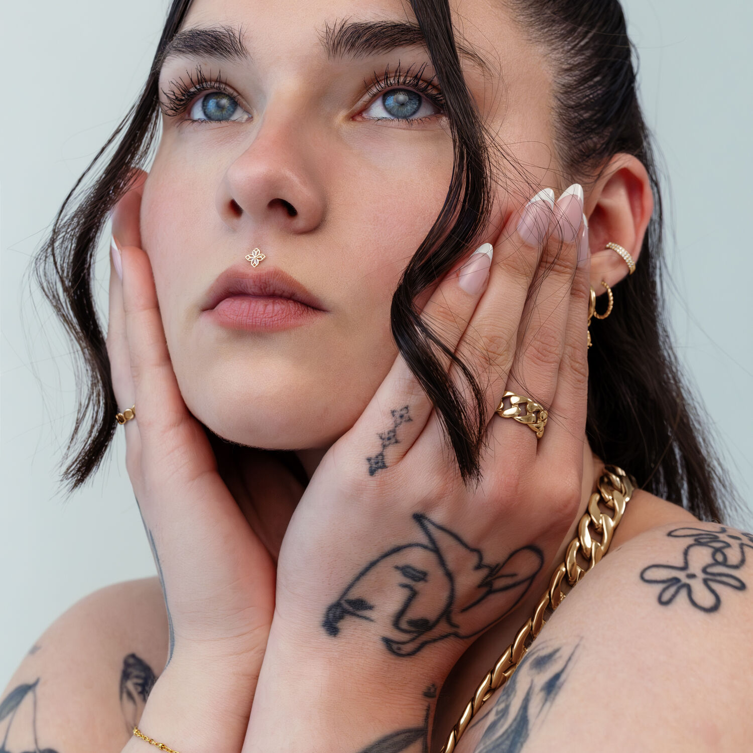 Mujer con piercing de aplique de flor dorada, tatuajes y joyas