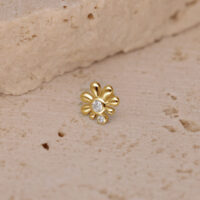 Ajuste de piercing dorado con piedras cristalinas sobre fondo color arena