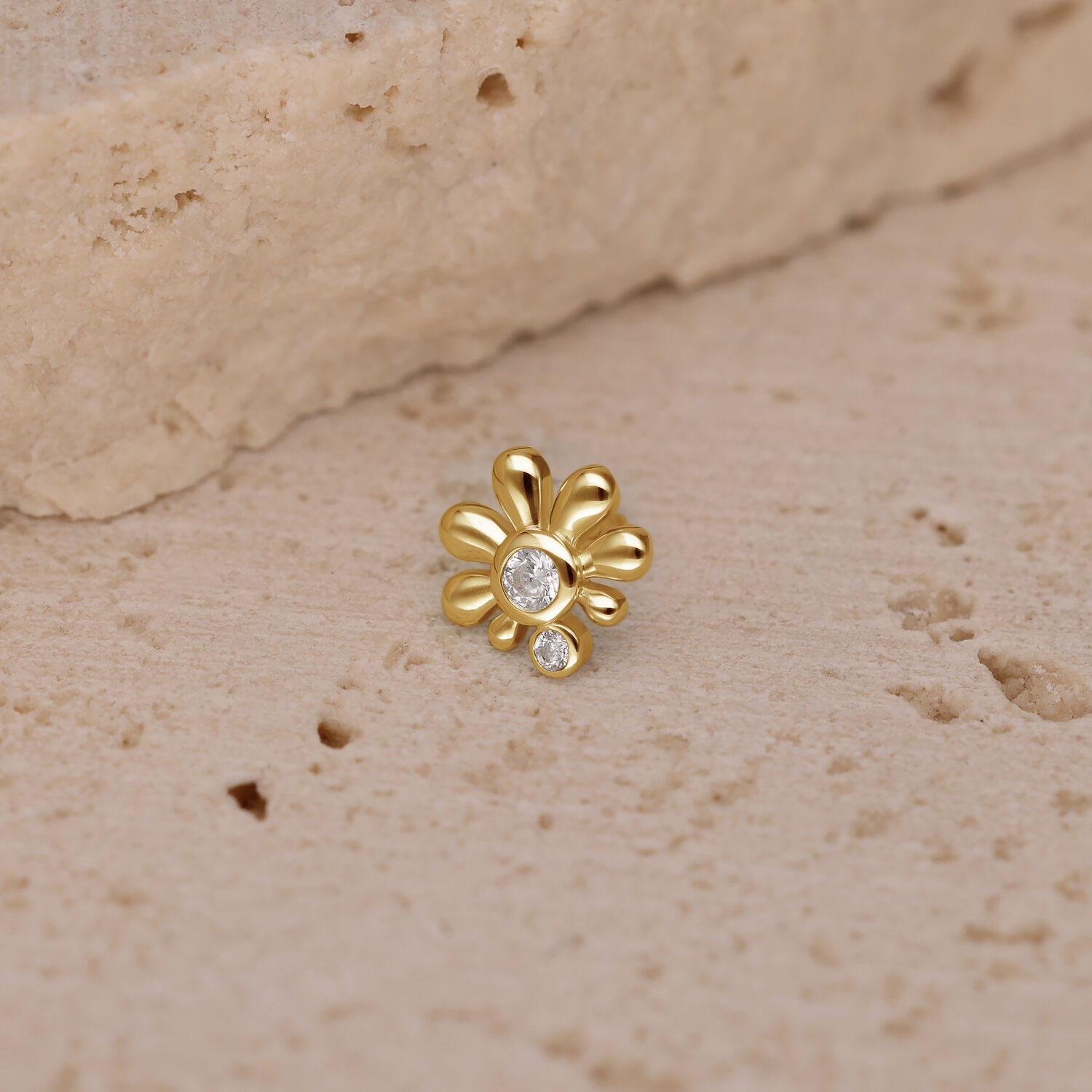Ajuste de piercing dorado con piedras cristalinas sobre fondo color arena