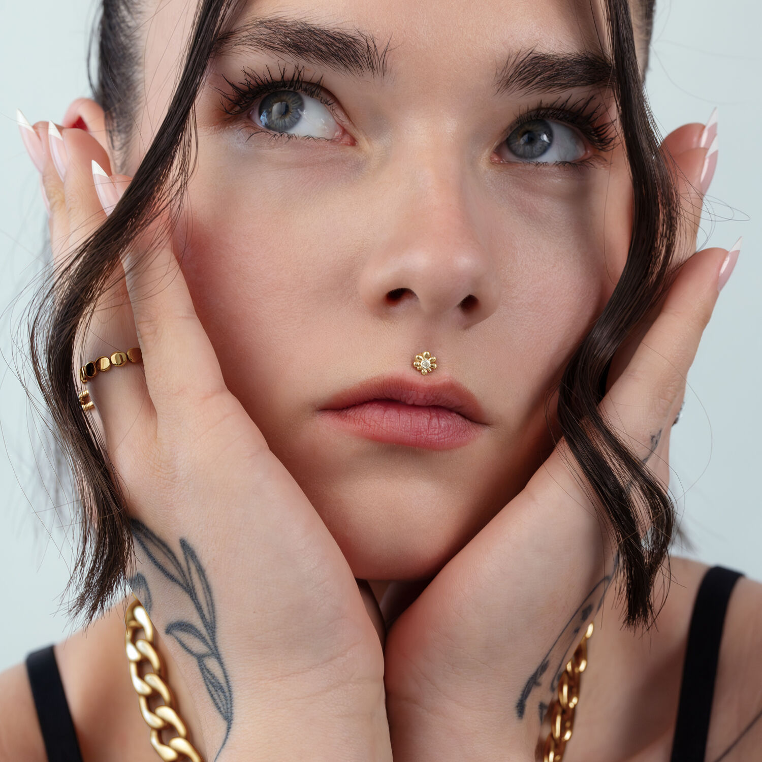 Mujer con piercing nasal dorado y tatuajes sobre fondo claro