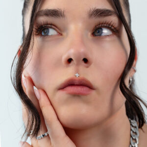 Primer plano de un rostro con un piercing de hoja plateada en la nariz, cabello al fondo