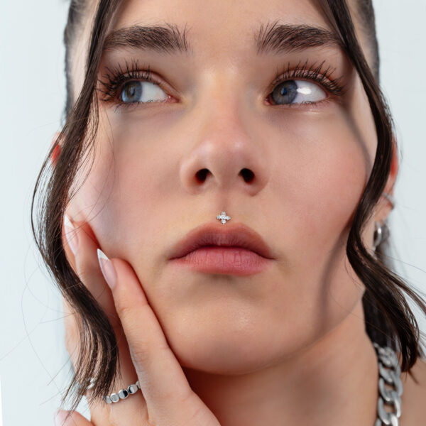 Primer plano de un rostro con un piercing de hoja plateada en la nariz, cabello al fondo