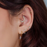 Oreja con varios piercings dorados, incluyendo un brillante accesorio en forma de arco