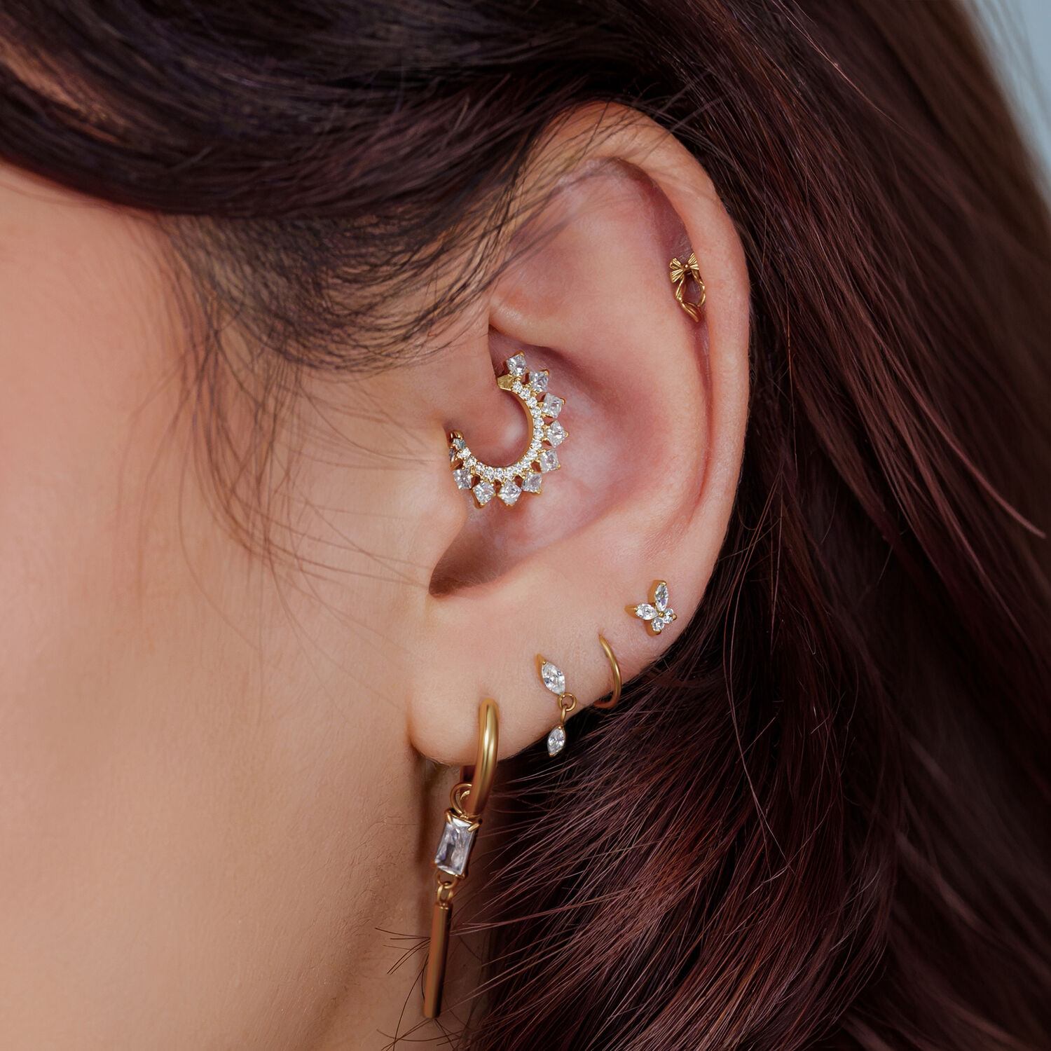 Oreja con varios piercings dorados, incluyendo un brillante accesorio en forma de arco