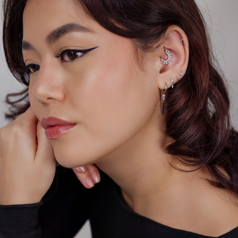 Mujer con varios piercings plateados, incluido un diseño en forma de luna en la oreja sobre fondo claro