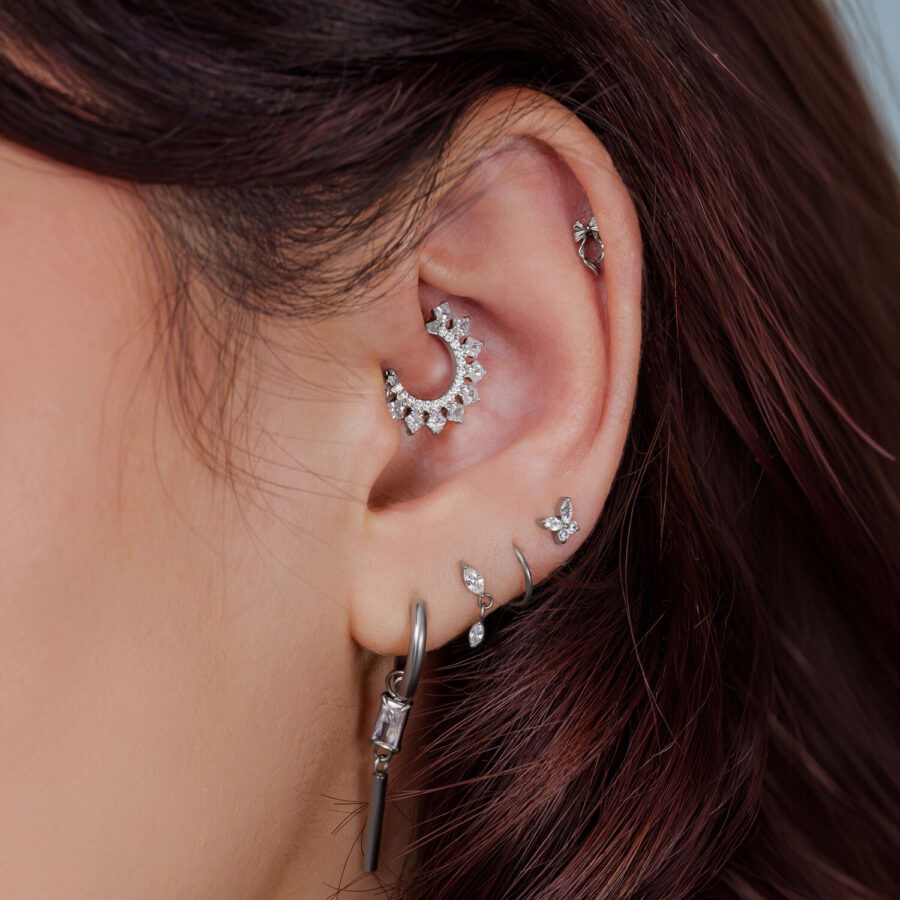 Primer plano de una oreja con varios accesorios de piercing plateados y joyas.