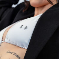 Primer plano de un top de bikini blanco con piercing Penta Crystal Barbell y tatuajes de fondo.