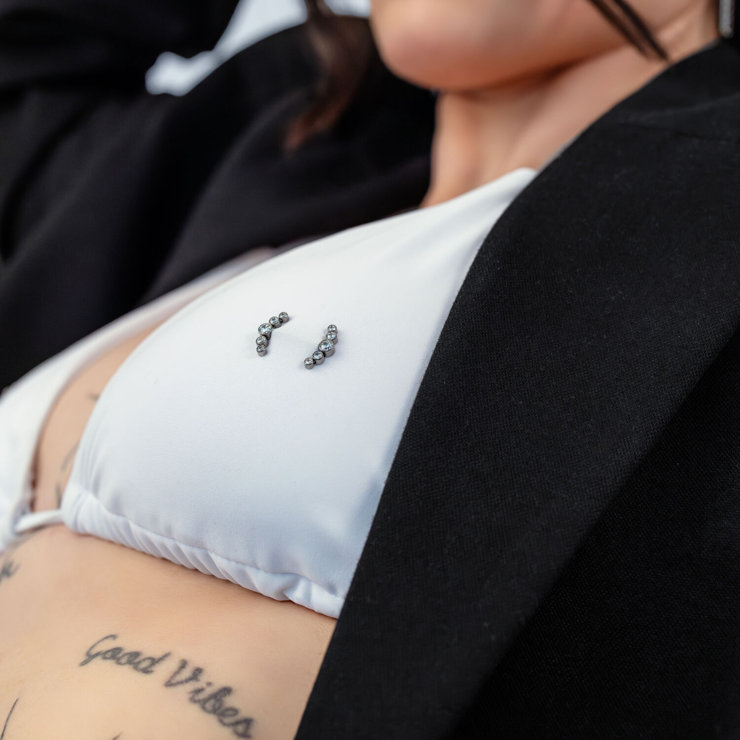 Primer plano de un top de bikini blanco con piercing Penta Crystal Barbell y tatuajes de fondo.