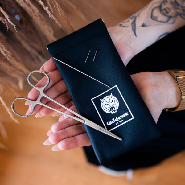 Estuche negro con logo de Wildcat, dos agujas y tijeras, sostenido en manos