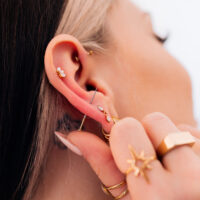 Piercings dorados en la oreja con joyas Primer plano de una oreja con varios piercings dorados y joyas, mano sosteniendo la oreja
