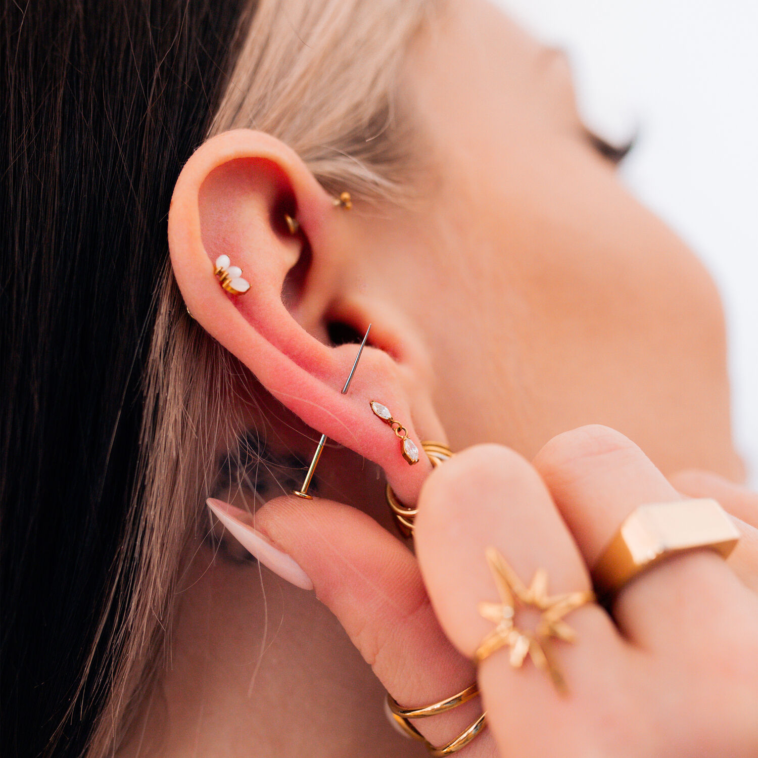 Piercings dorados en la oreja con joyas Primer plano de una oreja con varios piercings dorados y joyas, mano sosteniendo la oreja