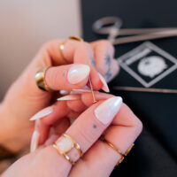 Set de Cambio de Piercing con Aguja Manos con uñas largas y blancas sostienen una aguja de piercing sobre un fondo negro