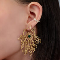 Pendientes dorados con diseño floral Primer plano de una oreja con pendientes dorados y acento verde sobre fondo claro