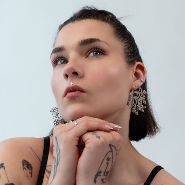 Mujer con pelo corto lleva grandes pendientes filigranas de metal plateado sobre fondo claro