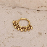 Anillo de piercing dorado con bolas sobre fondo beige texturizado