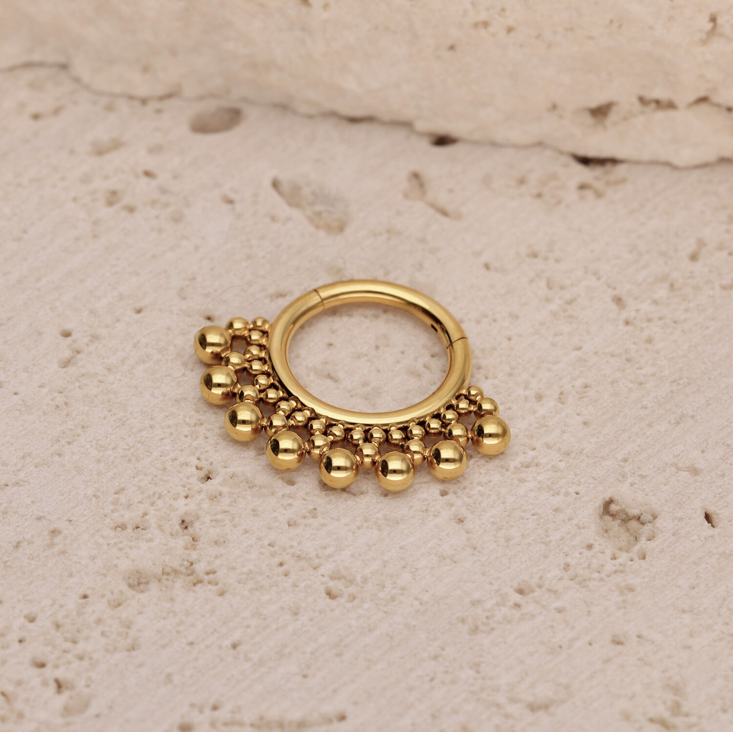 Anillo de piercing dorado con bolas sobre fondo beige texturizado