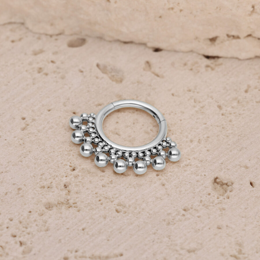 Clicker de septum plateado con pequeñas bolas sobre un fondo de piedra texturizada