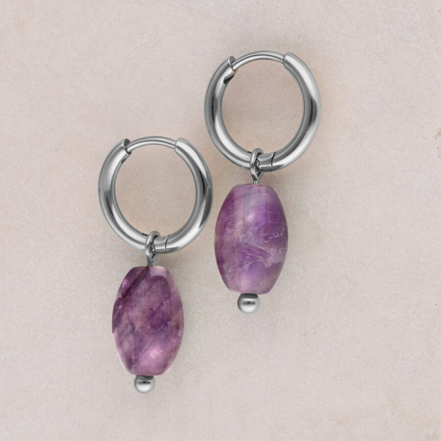 Dos aros de plata con colgante de amatista violeta sobre fondo beige