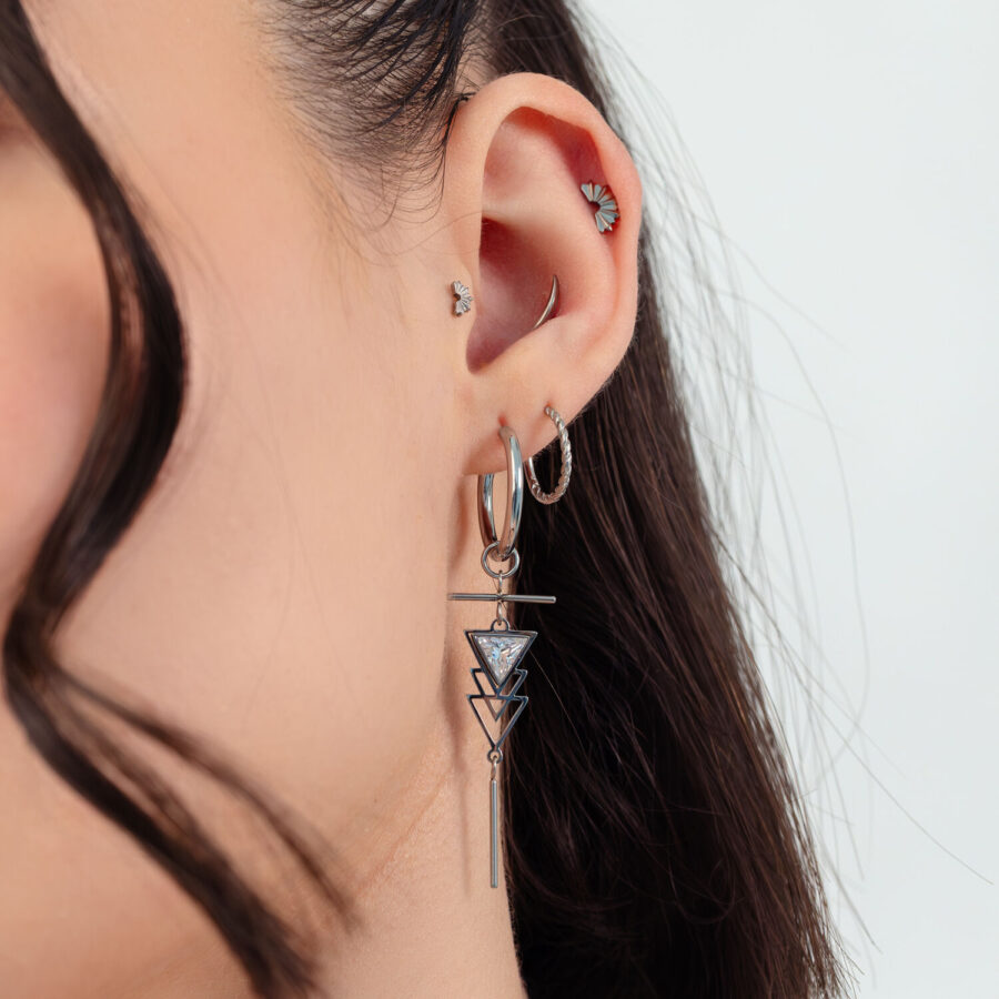 Mujer con pendientes Art Deco plateados y varios piercings en la oreja sobre fondo blanco