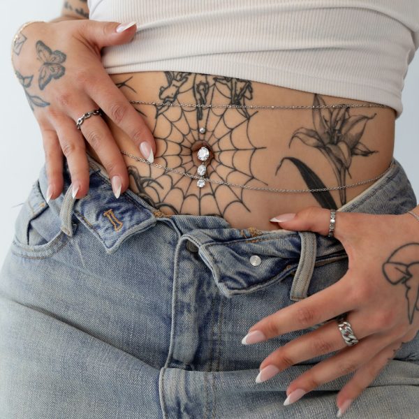Bananabell de tres cadenas con cristales en un vientre tatuado con jeans.
