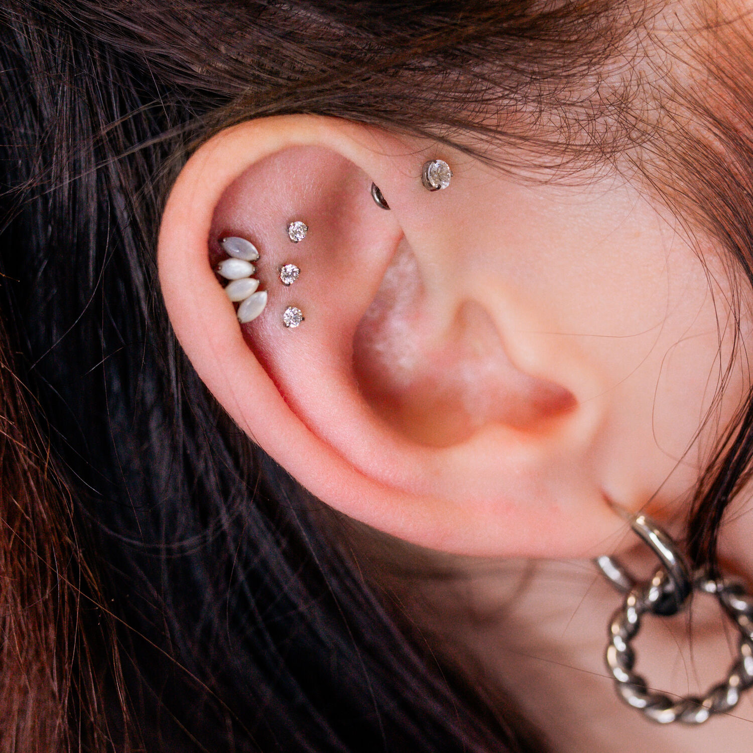 Primer plano de una oreja con varios piercings brillantes, incluido un Triple Labret Pushfit, sobre un fondo claro