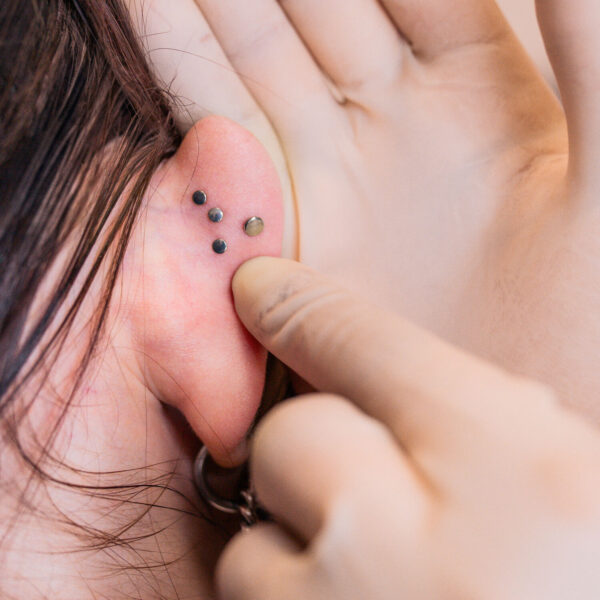 Primer plano de una oreja con tres labret piercings negros y un dedo tocando los piercings.