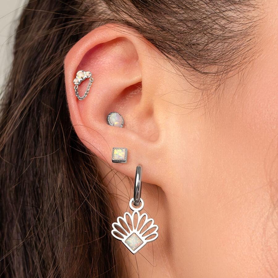 Primer plano de una oreja con varios piercings, incluido un piercing de ópalo con adorno de cadena