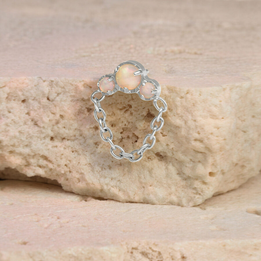 Piercing de ópalo en oro blanco con colgante de cadena sobre una piedra beige
