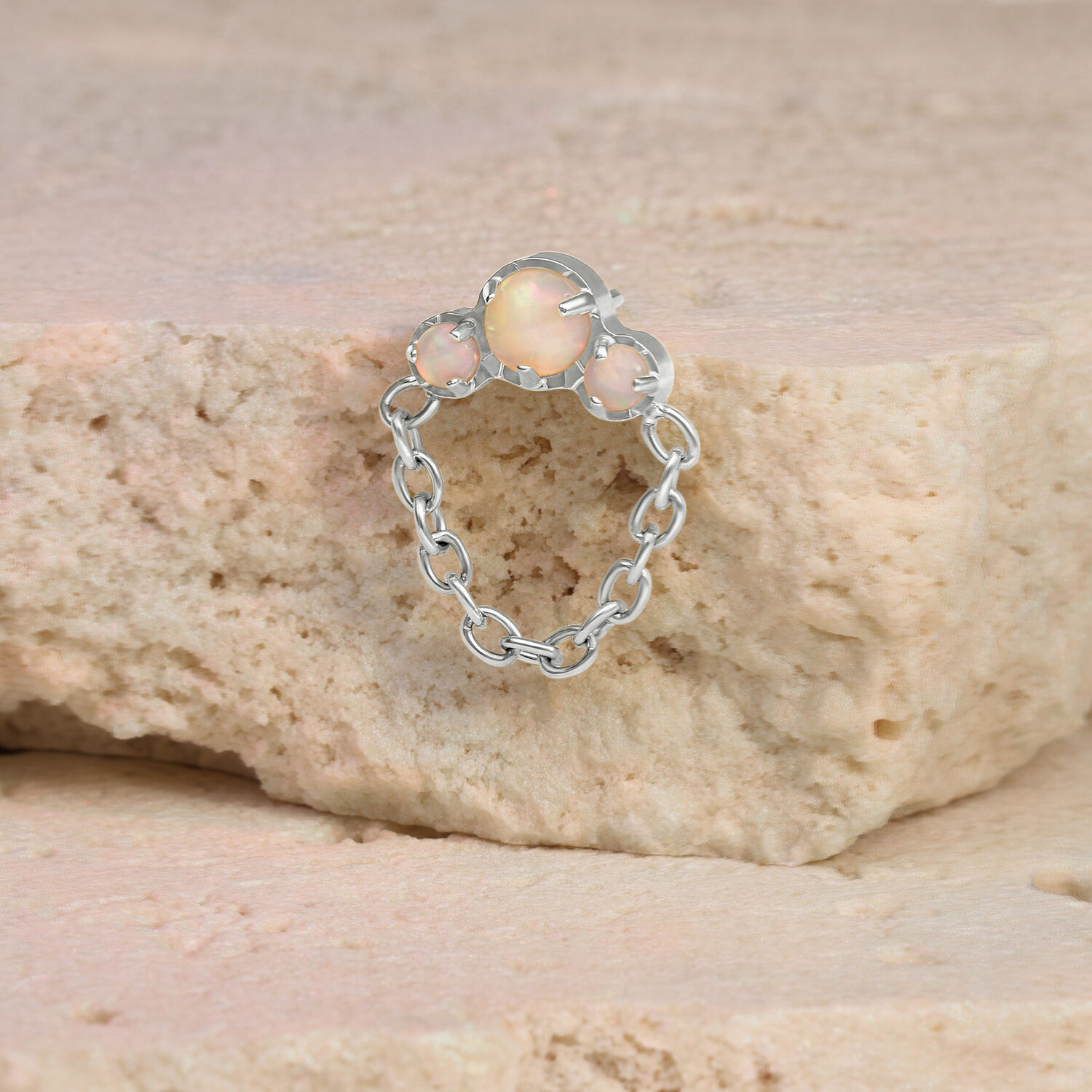 Piercing de ópalo en oro blanco con colgante de cadena sobre una piedra beige
