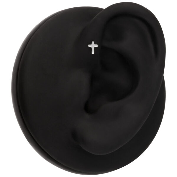 Modelo de oreja negra con piercing de cruz plateada sobre fondo negro