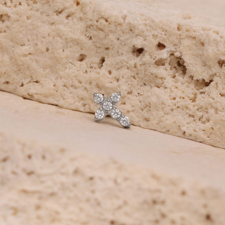 Pequeño accesorio de cruz de cristal plateado sobre superficie de piedra beige