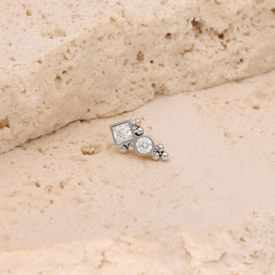 Adorno Push Fit plateado con cristales claros sobre superficie de piedra beige