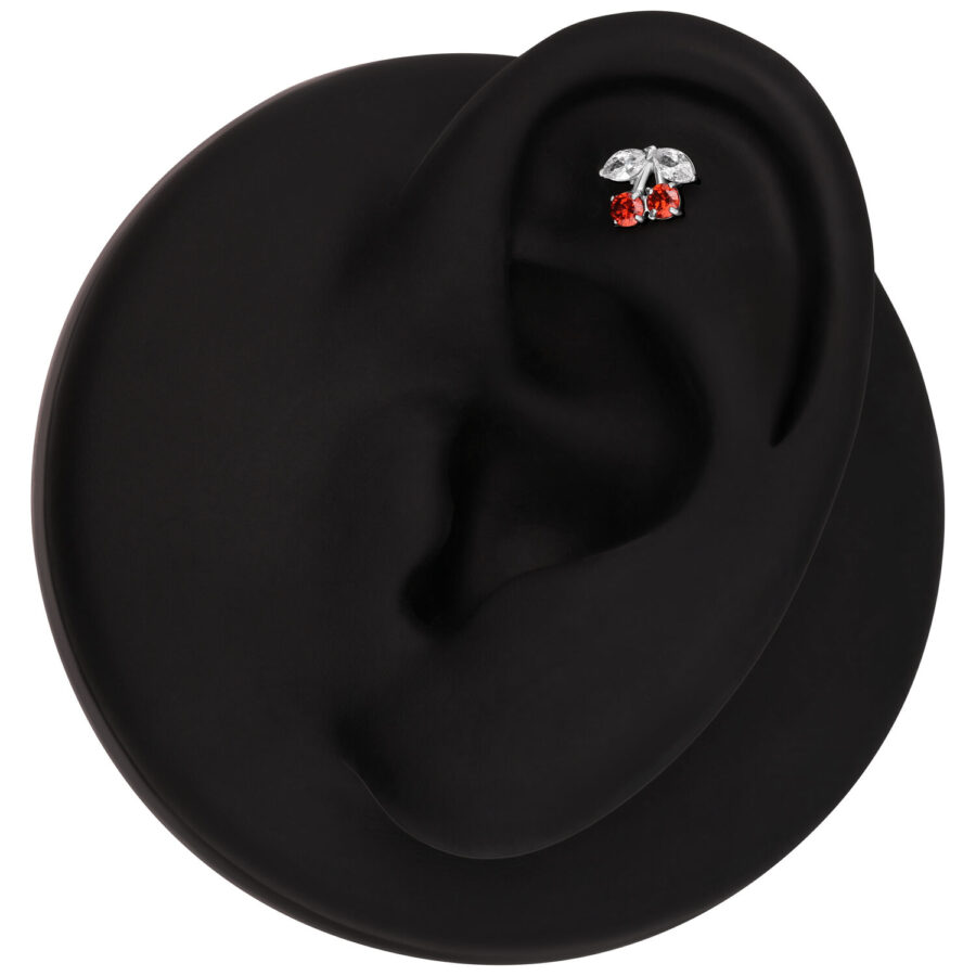 Modelo de oreja negra con accesorio de piercing plateado en forma de cereza y piedras rojas
