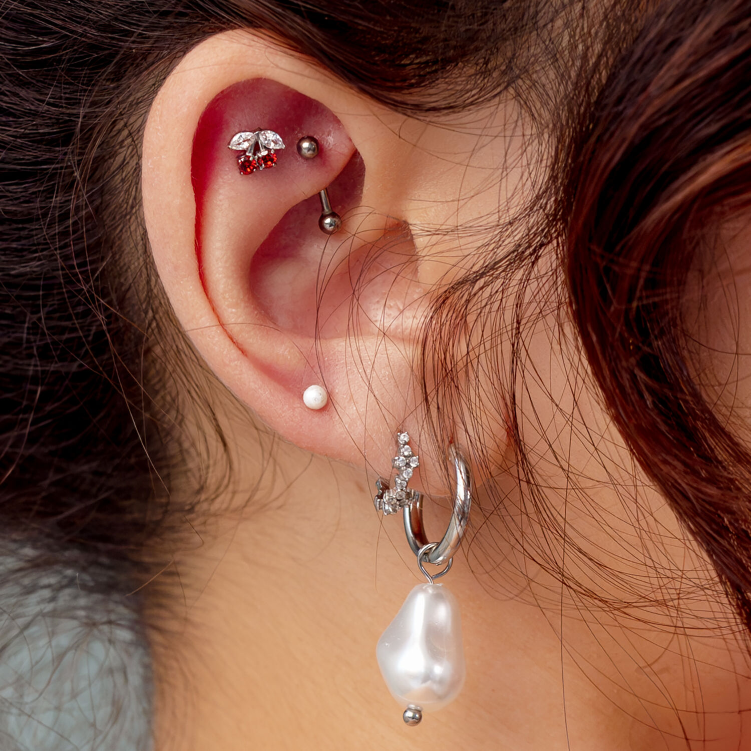 Accesorio de Cereza Push Fit Plateado Oreja con varios piercings, incluyendo un accesorio de cereza plateado con piedra roja