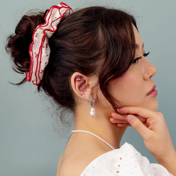 Mujer con cabello recogido, cinta roja y pendiente de perla frente a fondo gris